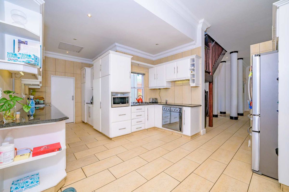 Spacious kitchen featuring white cabinetry, granite countertops, built-in appliances, and tiled flooring, seamlessly flowing into an open-plan area with a staircase and decorative columns.