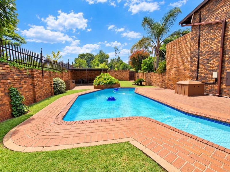 A well-maintained outdoor pool area featuring a swimming pool, brick paving, and secure face brick boundary walls with electric fencing.