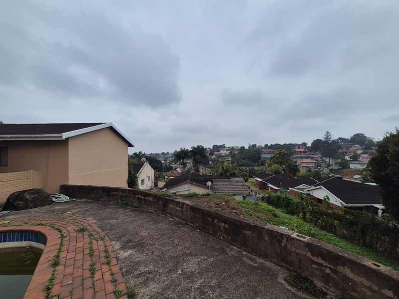 Elevated view overlooking the surrounding residential neighborhood, featuring a swimming pool area with a retaining wall and brick paved surround.