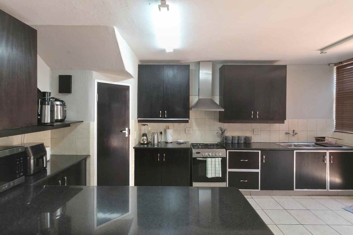 A functional kitchen featuring dark cabinetry, granite countertops, a stainless steel extractor fan, and tiled flooring.