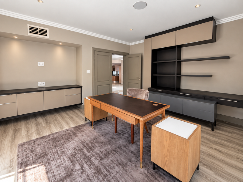 A modern, well-appointed home office featuring custom built-in cabinetry, integrated shelving, recessed lighting, and high-quality laminate flooring.