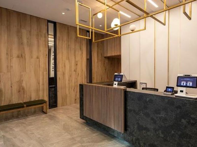 Modern office building reception area featuring a stone reception desk, wood-paneled walls, and contemporary pendant lighting.