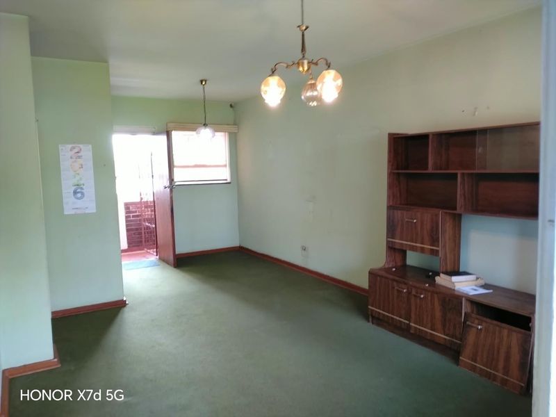 A living room area featuring green carpet flooring and ceiling light fixtures, offering a blank canvas for potential renovation and modernization.