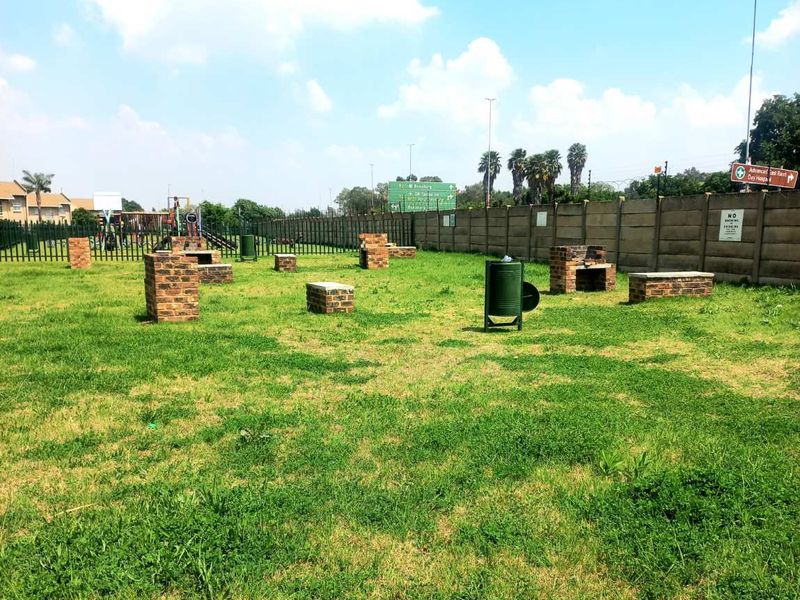Communal garden area featuring multiple brick braai stands, enclosed by perimeter walls and metal fencing.