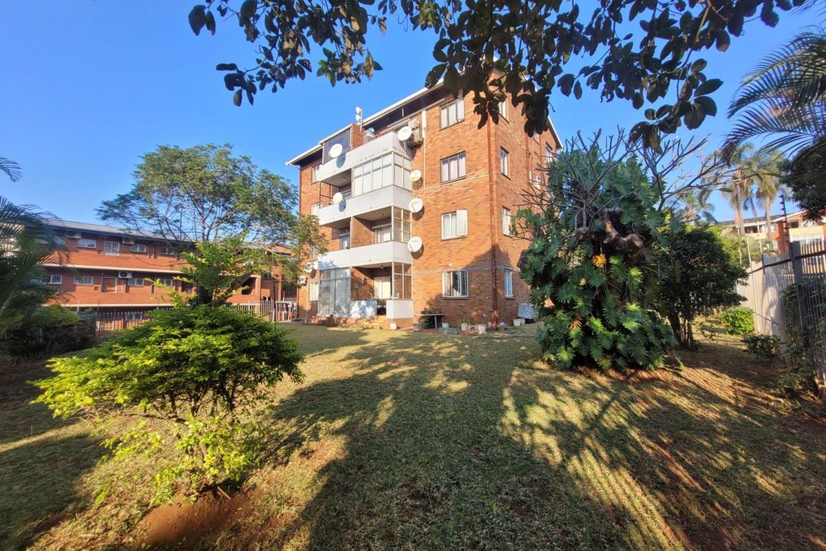 Rear view of a multi-story brick apartment building featuring enclosed balconies and a well-maintained communal garden area.