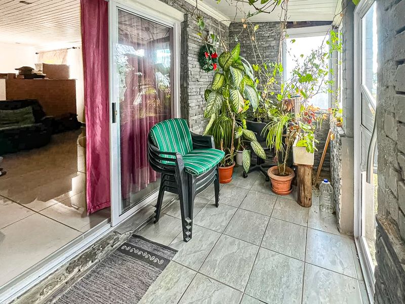 A covered patio area featuring tiled flooring, stone-clad feature walls, and sliding glass doors providing access to the interior living space.