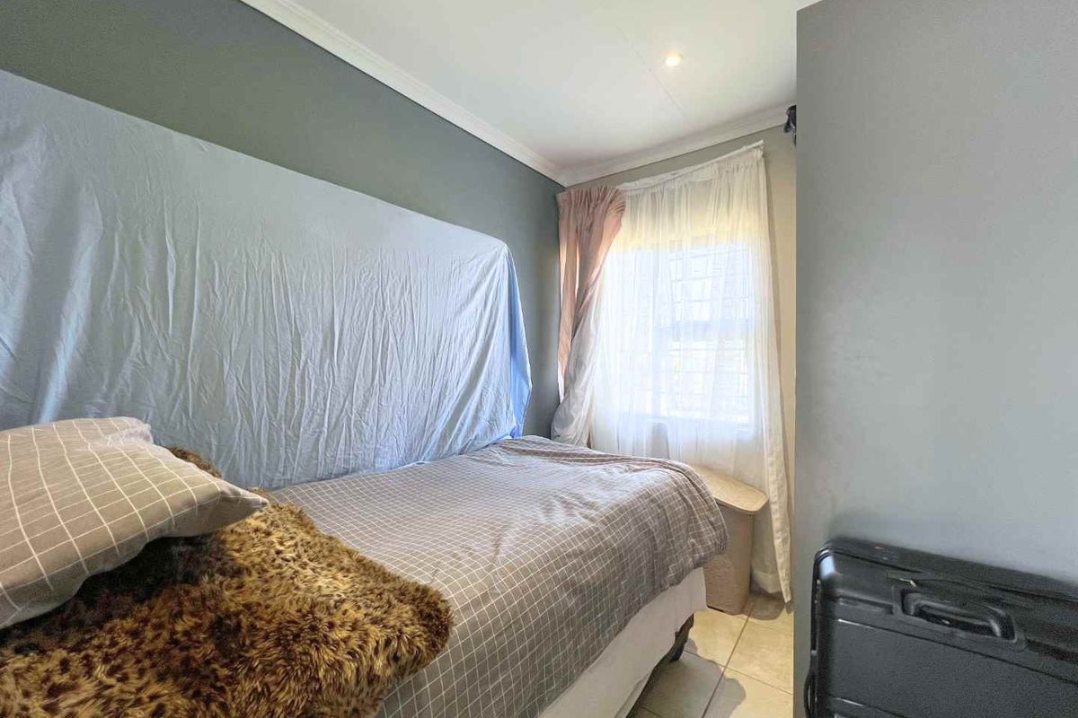 A compact bedroom featuring tiled flooring, neutral wall finishes, and a window with fitted curtain tracks.