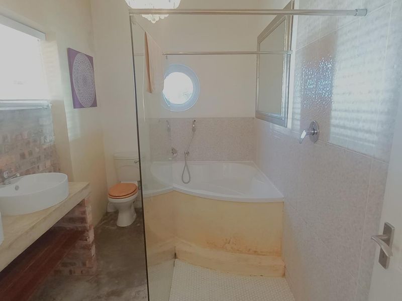 Bathroom featuring a double vanity with vessel sinks, a corner bathtub with a glass screen, and a unique porthole window.