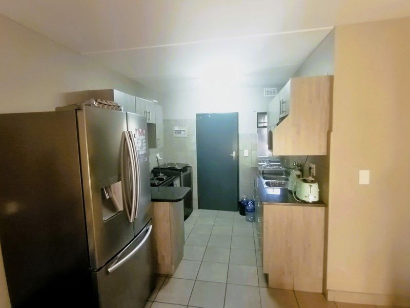 A functional kitchen featuring light wood-finish cabinetry, laminate countertops, tiled flooring, and a double sink, providing a practical workspace.