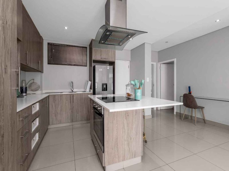 Modern kitchen featuring wood-finish cabinetry, stone countertops, a central island with a built-in hob and oven, and high-quality stainless steel appliances.
