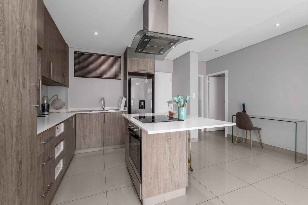 Modern kitchen featuring wood-finish cabinetry, stone countertops, a central island with a built-in hob and oven, and high-quality stainless steel appliances.