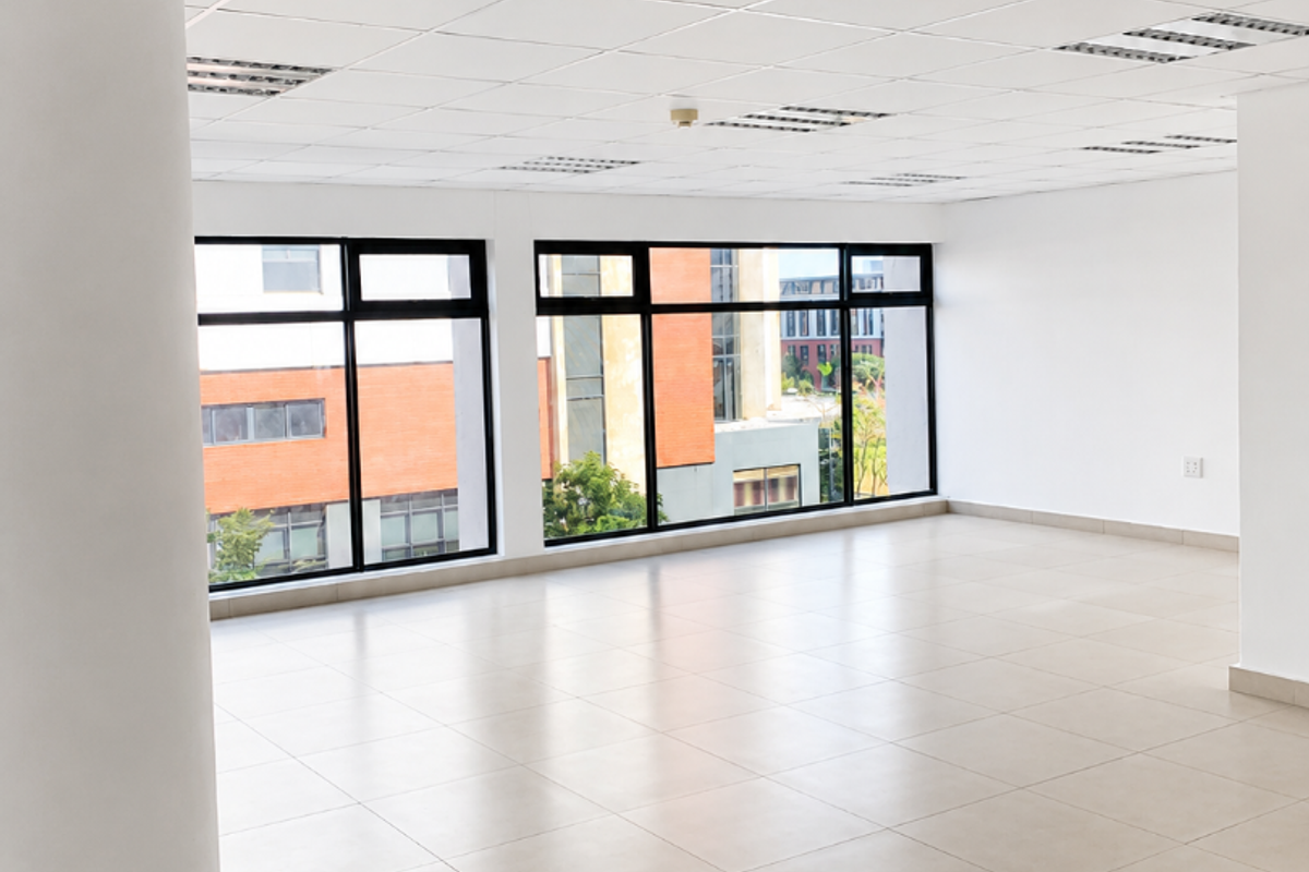 A bright, open-plan office space featuring large windows, neutral ceramic floor tiles, and a suspended ceiling with integrated lighting.