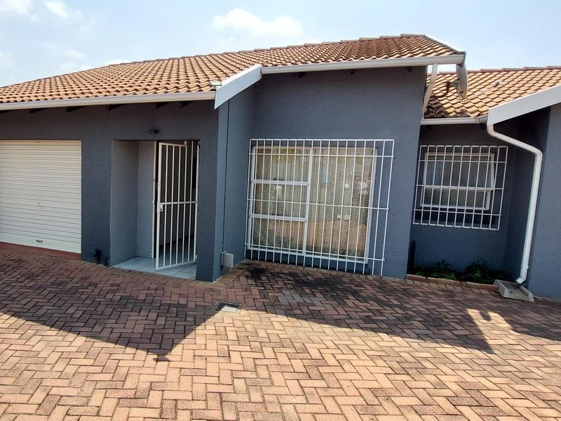 Front elevation of a townhouse featuring a paved driveway, single garage with roller door, and security bars on windows and entrance.