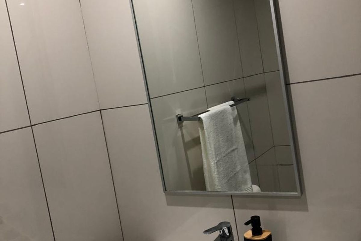 A modern bathroom vanity featuring a white ceramic basin, chrome faucet, and a sleek wall-mounted mirror with tiled splashback.