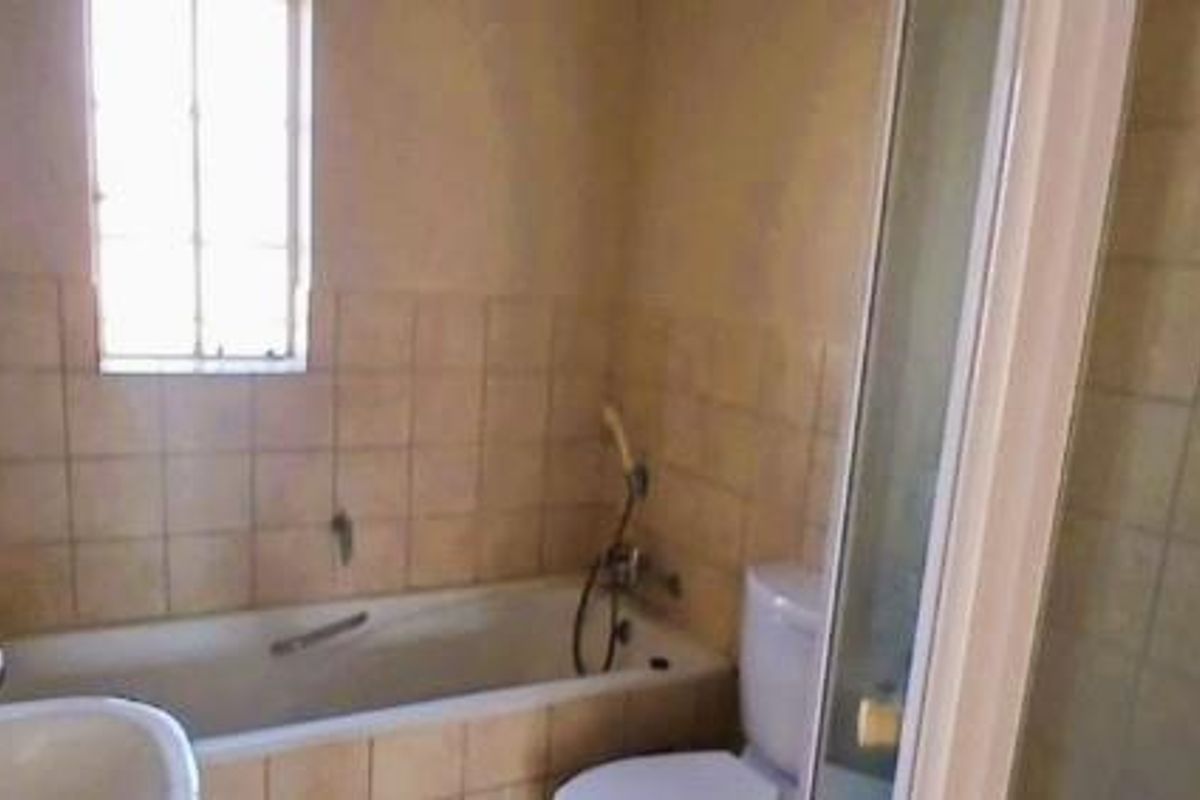 A dated bathroom featuring a built-in bathtub, separate shower enclosure, and toilet, with neutral wall tiling and a small window for natural light.