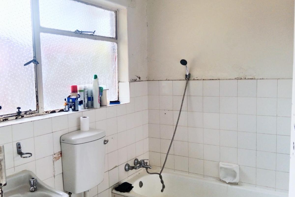 A dated bathroom featuring a bathtub with handheld shower, wall-mounted basin, and toilet, requiring significant renovation and cosmetic updates to improve its condition.
