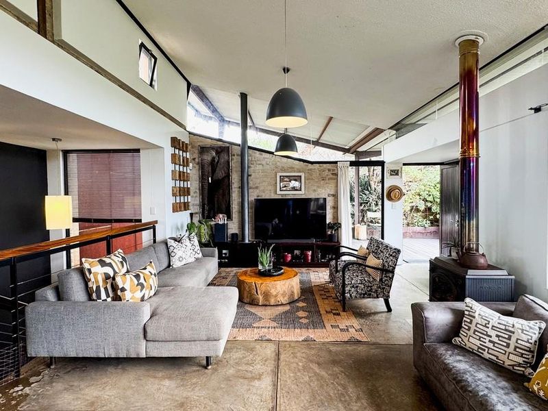 Spacious living room featuring a striking exposed stone wall, a modern wood-burning fireplace, polished concrete floors, and high vaulted ceilings with clerestory windows.