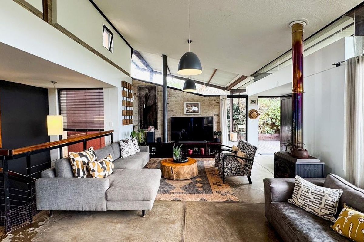 Spacious living room featuring a striking exposed stone wall, a modern wood-burning fireplace, polished concrete floors, and high vaulted ceilings with clerestory windows.