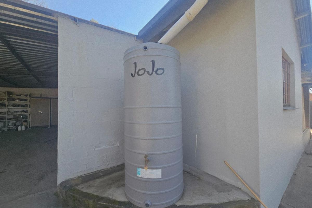 Exterior view showing a grey plastic water storage tank connected to the building's gutter system, situated on a concrete base.