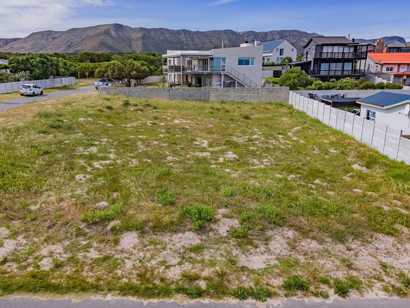 An elevated view of a vacant residential plot featuring natural vegetation and surrounding boundary walls in a developed coastal neighborhood.