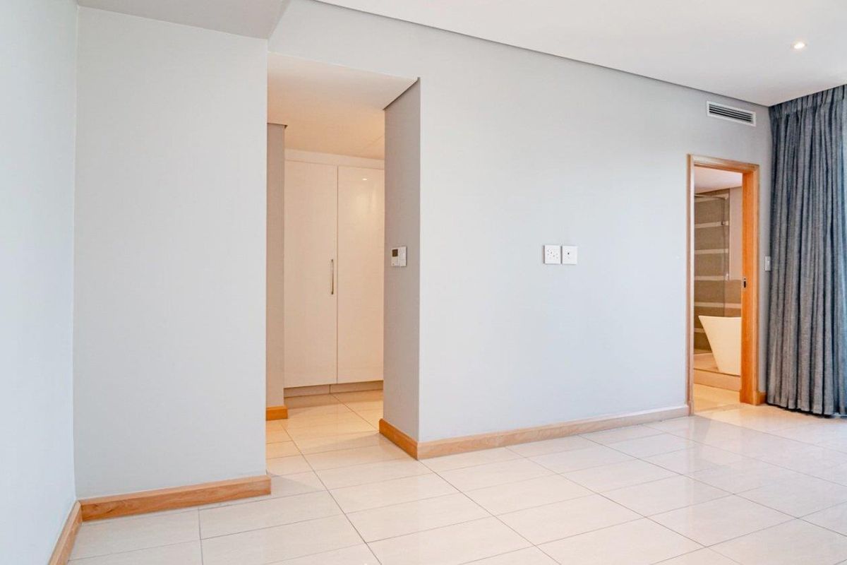 A bright, modern bedroom featuring tiled flooring, built-in cupboards, and direct access to an en-suite bathroom and a private balcony.