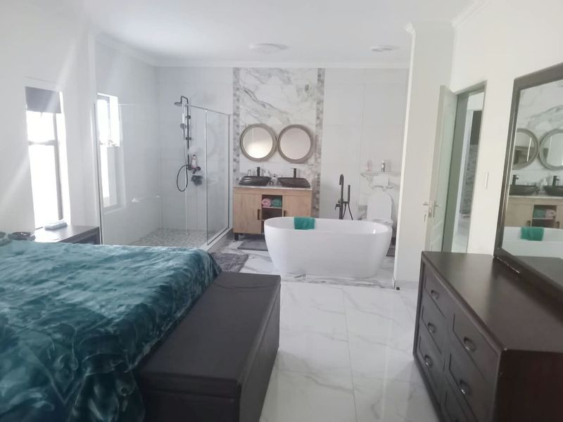 Spacious bedroom featuring an integrated open-plan en-suite bathroom with a modern freestanding bathtub, glass shower, and double vanity with marble-style finishes.