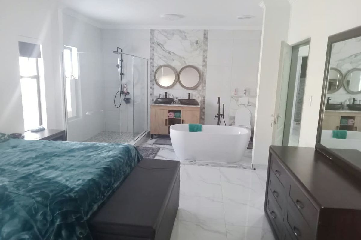 Spacious bedroom featuring an integrated open-plan en-suite bathroom with a modern freestanding bathtub, glass shower, and double vanity with marble-style finishes.