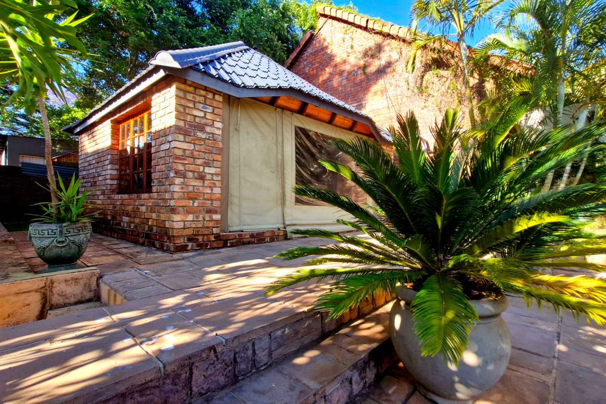 A charming brick-built garden structure featuring a tiled roof and canvas-style side panels, set within a landscaped outdoor area with paved patio space.