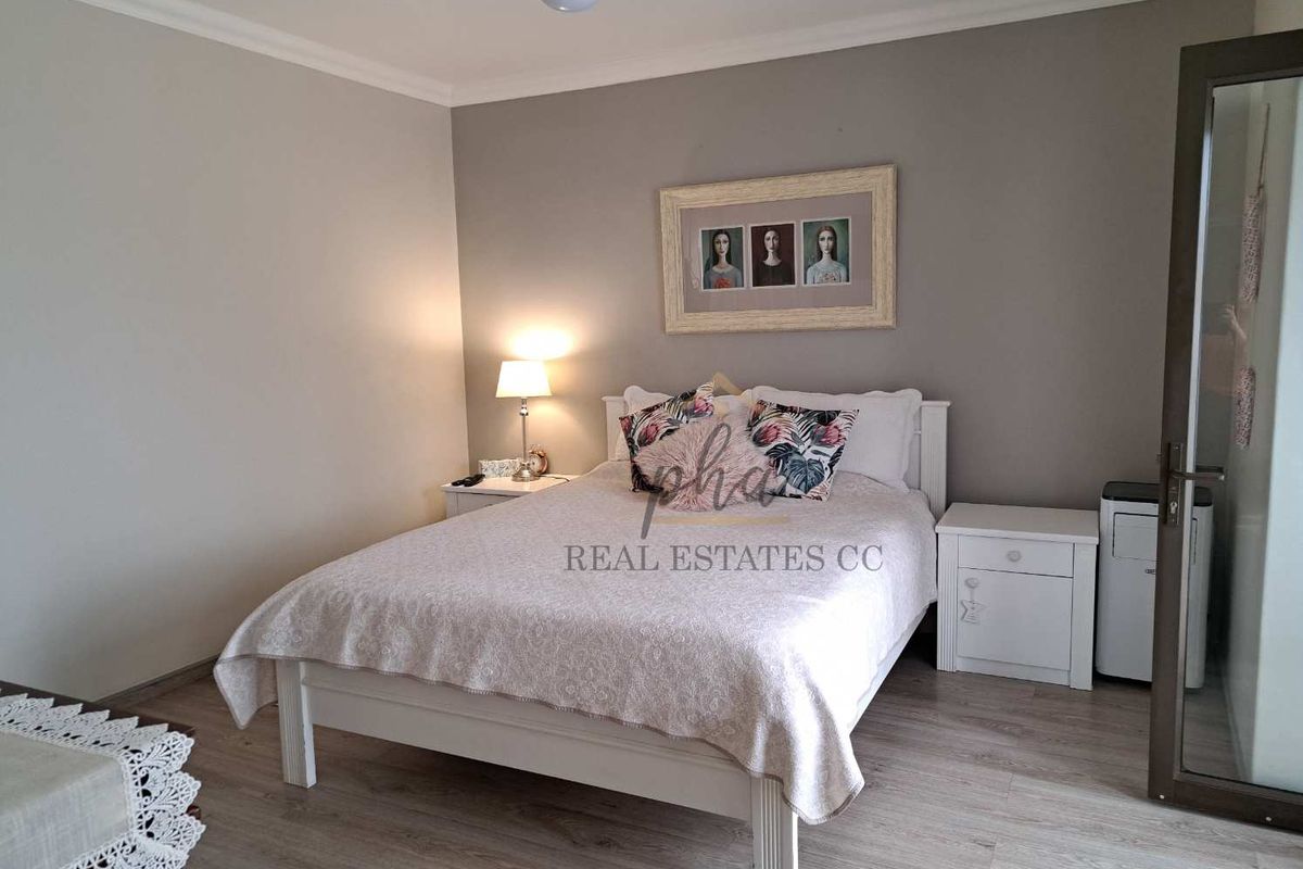 A well-maintained bedroom featuring light wood-look laminate flooring, neutral wall tones, and a ceiling fan.