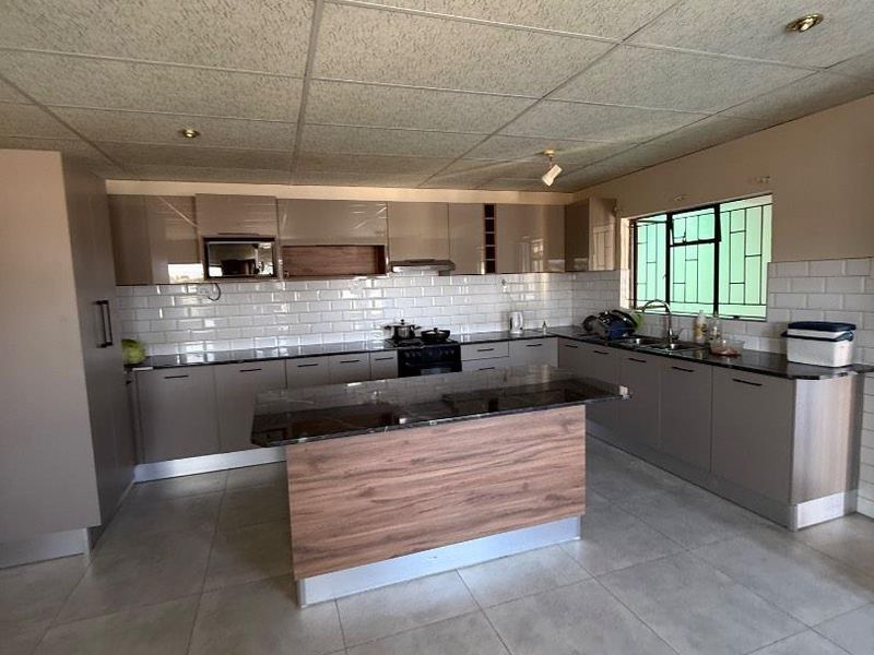 Modern kitchen featuring sleek cabinetry, a central island with stone countertops, subway tile backsplash, and tiled flooring throughout.