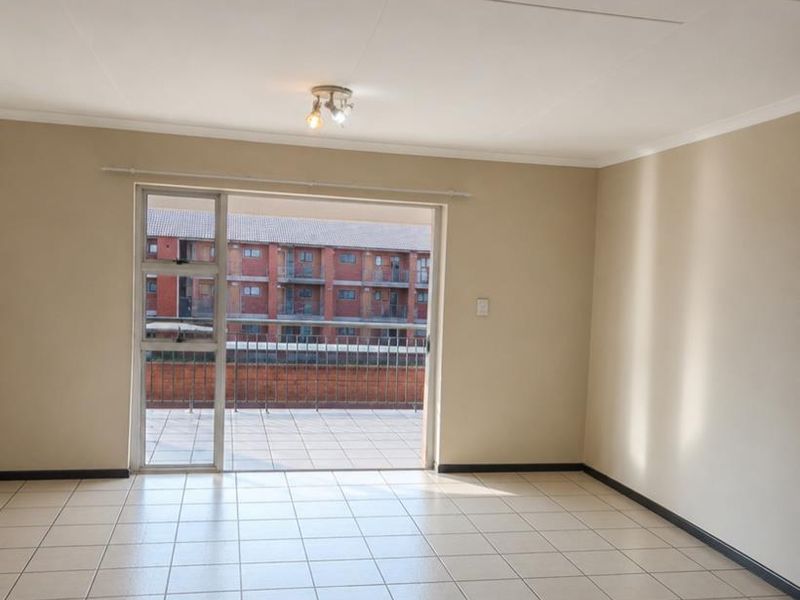 A bright, empty living room featuring neutral tiled flooring and a large sliding glass door providing access to an outdoor balcony area.