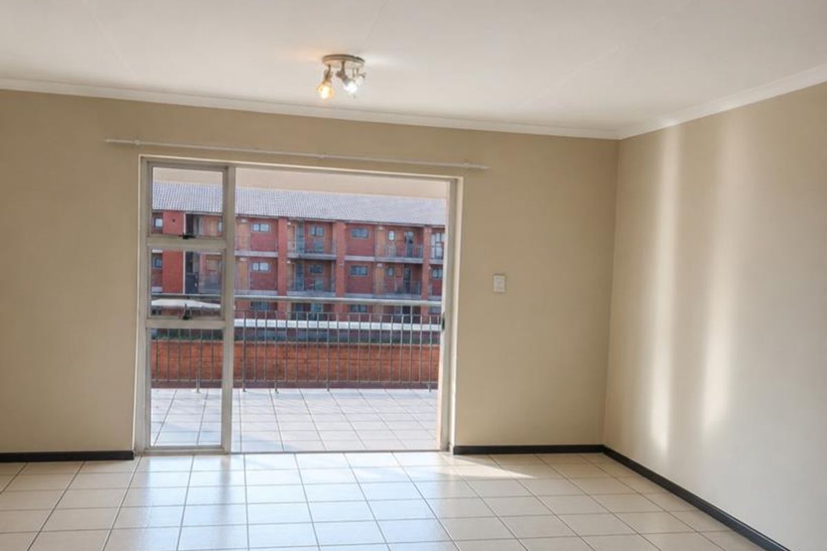 A bright, empty living room featuring neutral tiled flooring and a large sliding glass door providing access to an outdoor balcony area.