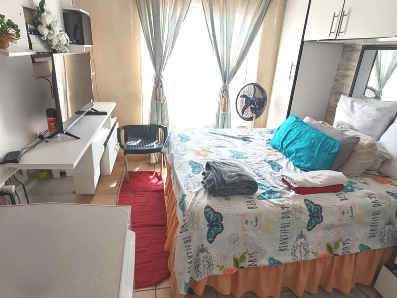 A compact bedroom featuring built-in cupboards and tiled flooring, offering a functional living space with natural light from the window.