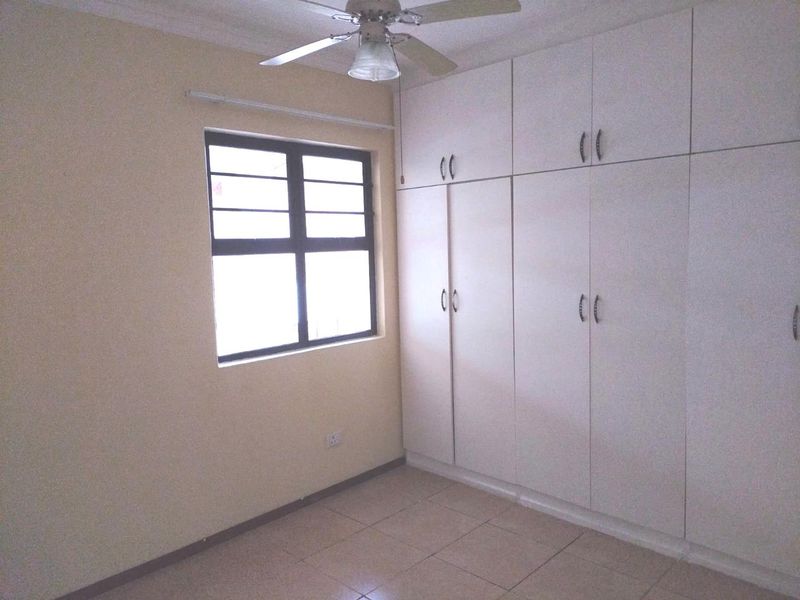 A clean, empty bedroom featuring neutral tiled flooring, a ceiling fan, and ample built-in cupboard storage space.