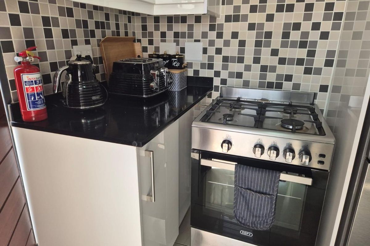 Compact kitchen area featuring a stainless steel gas stove, black granite countertops, and a modern mosaic tile backsplash.