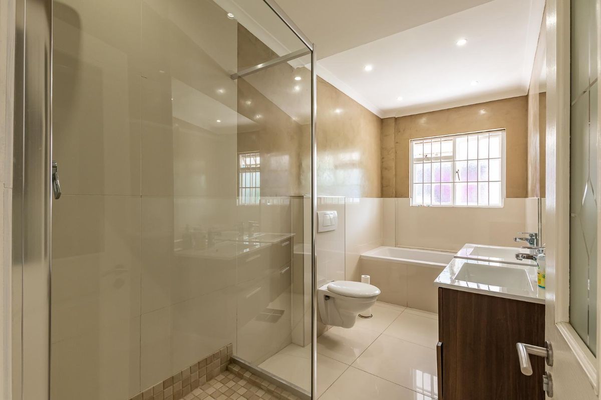 Modern bathroom featuring a glass-enclosed shower, wall-mounted toilet, double vanity with integrated sinks, and a built-in bathtub with tiled finishes.