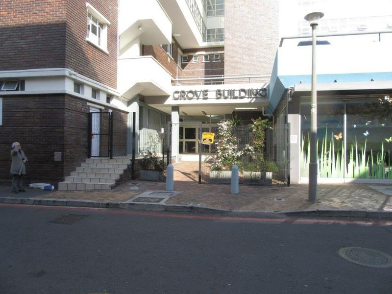 Street-level view of the Grove Building entrance, featuring a brick facade, paved access area, and secure gated entry.