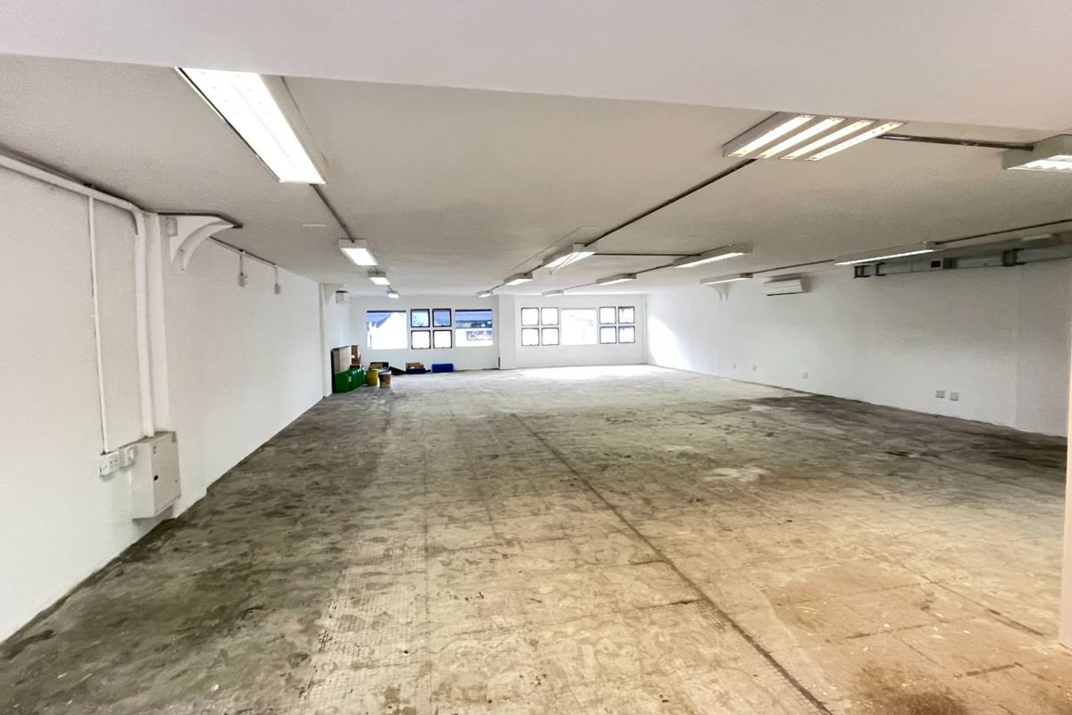 A large, open-plan retail or commercial space featuring white walls, fluorescent lighting, air conditioning, and unfinished concrete flooring, ready for custom fit-out.