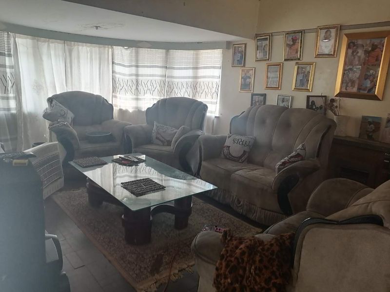 A living room area featuring a large window with curtains and visible signs of ceiling water damage requiring maintenance.