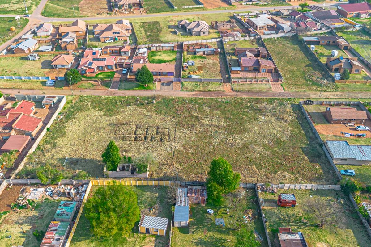Aerial view of a residential neighborhood featuring a large vacant plot of land surrounded by established housing and perimeter fencing.