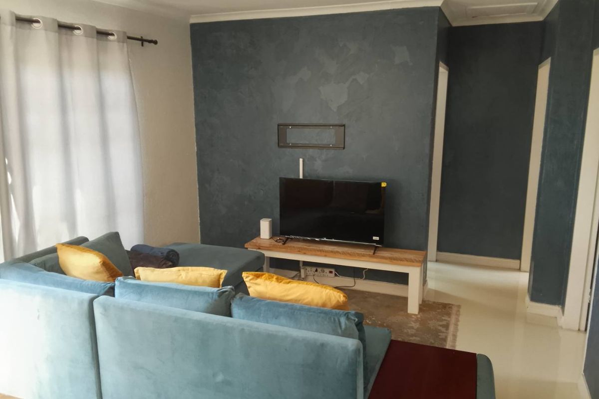 A comfortable living room featuring a textured dark blue feature wall, tiled flooring, and classic cove cornicing, creating a modern and inviting atmosphere.