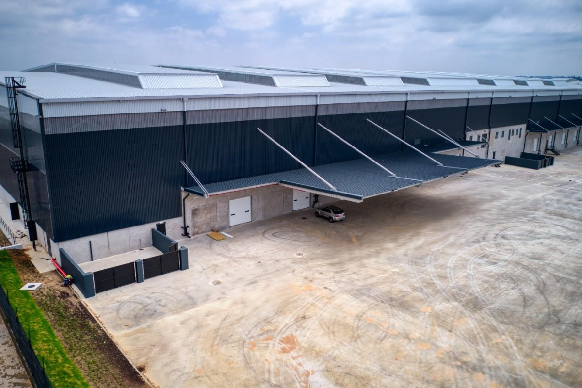 Aerial view of a modern industrial warehouse facility featuring extensive metal cladding, a large loading canopy, and a spacious concrete yard.