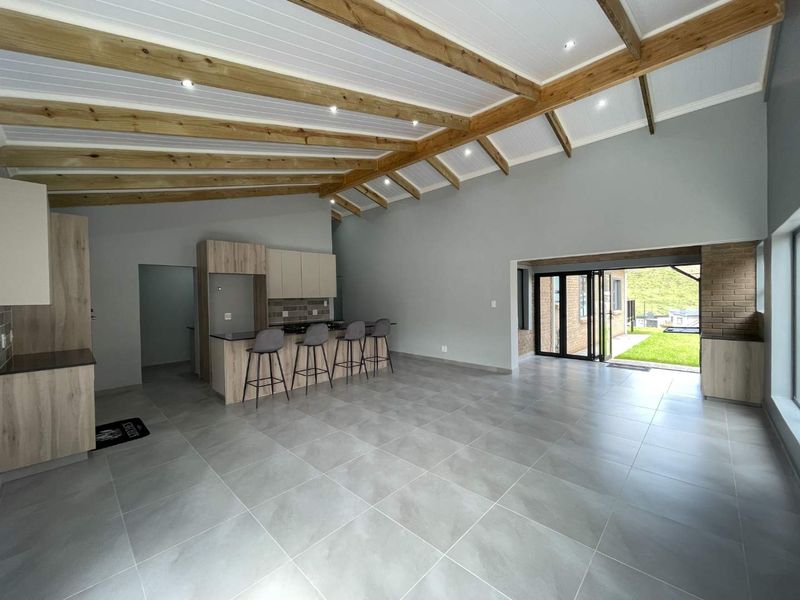 Spacious open-plan living and kitchen area featuring high vaulted ceilings with exposed timber beams, modern tiled flooring, and seamless access to the rear garden.