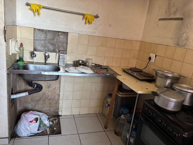 A compact kitchen area featuring a stainless steel sink, electric hob, and oven, currently requiring significant maintenance and cosmetic repairs to the wall finishes.