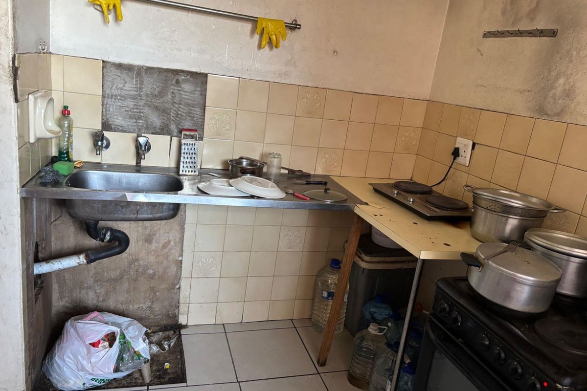 A compact kitchen area featuring a stainless steel sink, electric hob, and oven, currently requiring significant maintenance and cosmetic repairs to the wall finishes.