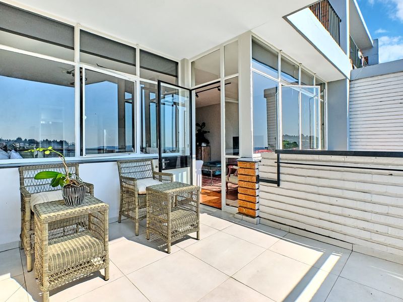 A bright, tiled penthouse balcony featuring aluminium-framed windows and doors, offering a seamless transition to the interior living space.