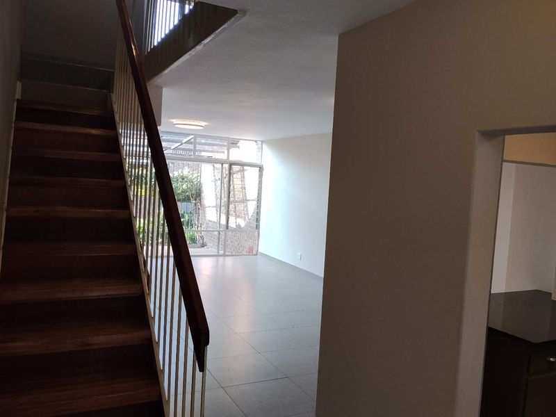 An open-plan living area featuring tiled flooring, a timber staircase with metal balustrade, and large sliding glass doors leading to the rear exterior.