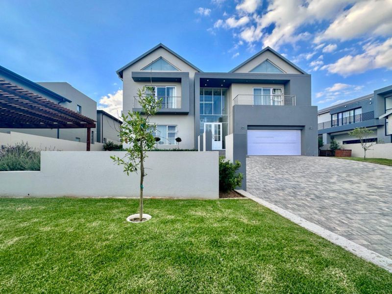 Modern double-story residential home featuring a paved driveway, double garage, and upper-level balconies with contemporary architectural design.