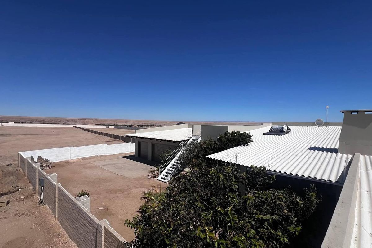 Aerial view of the property showing the corrugated metal roof, solar water heating system, external staircase, and surrounding fenced yard area.