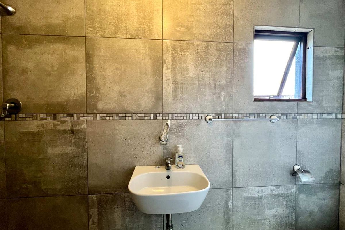 A modern bathroom featuring large-format grey wall tiles, a wall-mounted basin, and a shower fixture with a top-hung window for natural light.